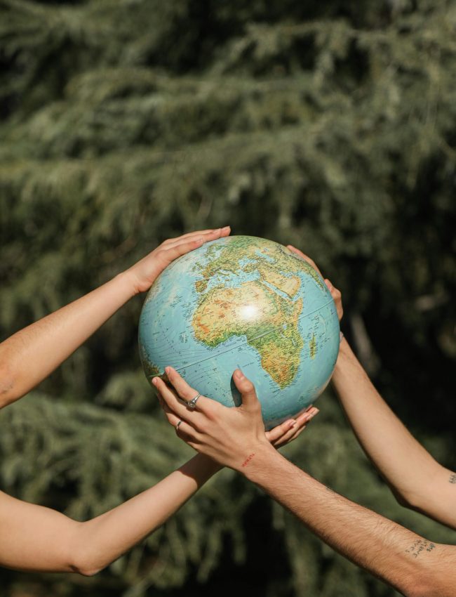 Four hands holding a globe outdoors, symbolizing unity and environmental conservation.